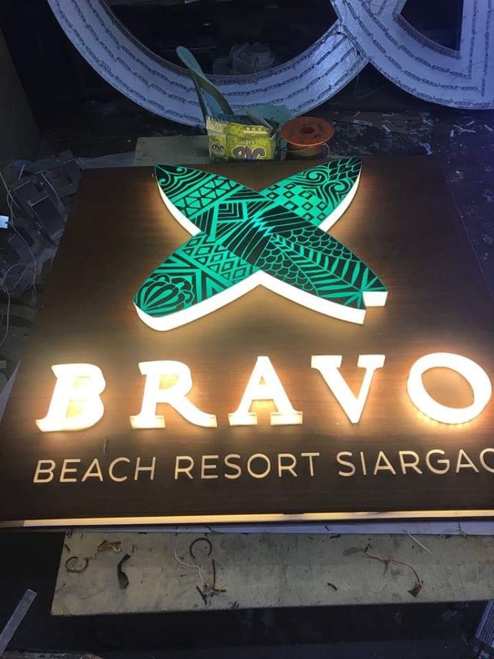 Illuminated outdoor signage for BRAVO BEACH RESORT SIARGAO in Makati with green X, dark background, by M&G Global Ads.
