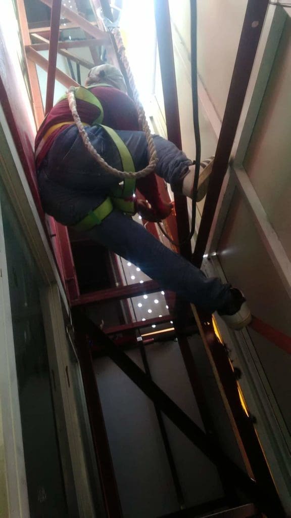 Worker in harness climbs beams with caution billboard signage in background, Quezon City location, by M&G Global Ads.