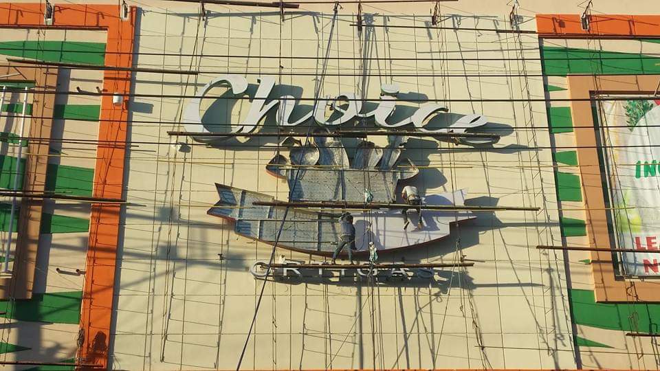 Workers install a Choice fish graphic pylon signage on a building in Makati, with scaffolding; by M&G Global Ads.