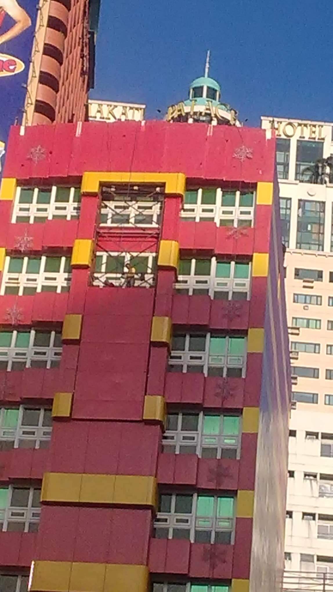 Outdoor signage on a red and yellow building near a white hotel in Makati, by M&G Global Ads.