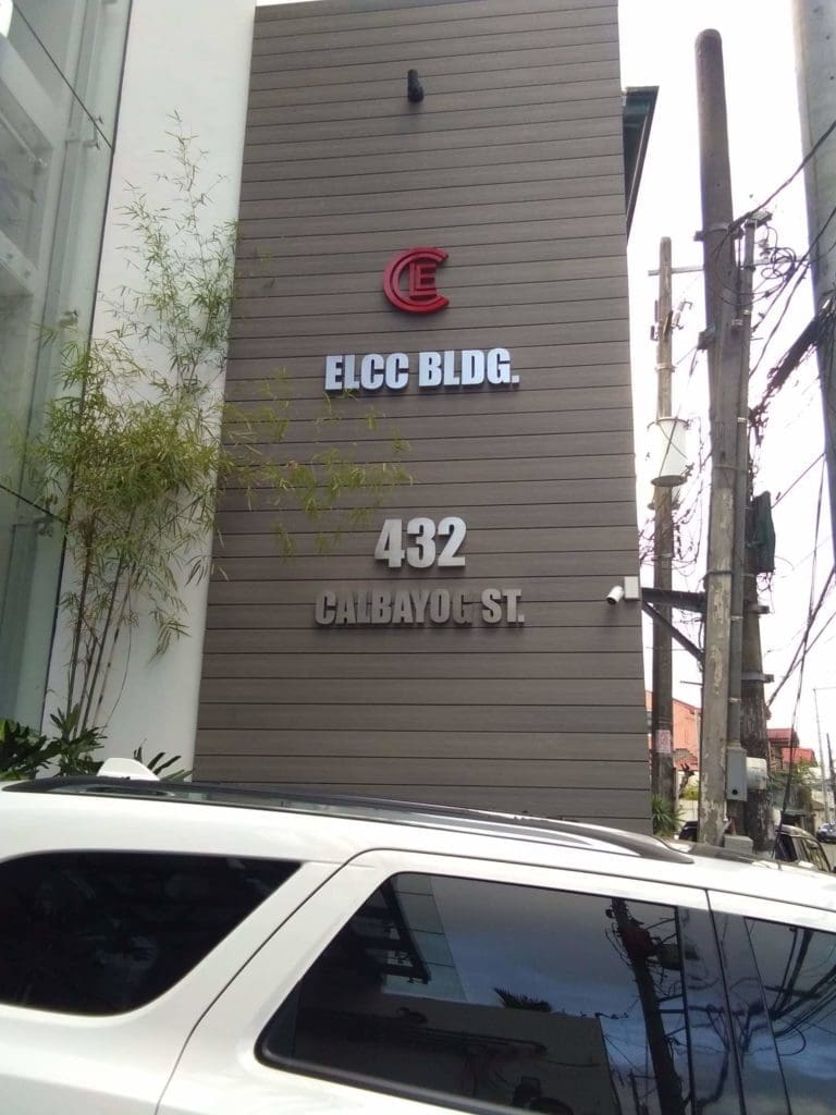 Metallic outdoor signage for ELCC BLDG. 432 Calbayog St. in Quezon City, with SUV and greenery, by M&G Global Ads.