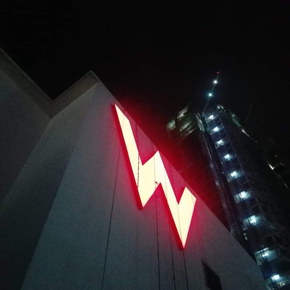Illuminated W acrylic signage installation in Makati at night with high-rise under construction, by M&G Global Ads.