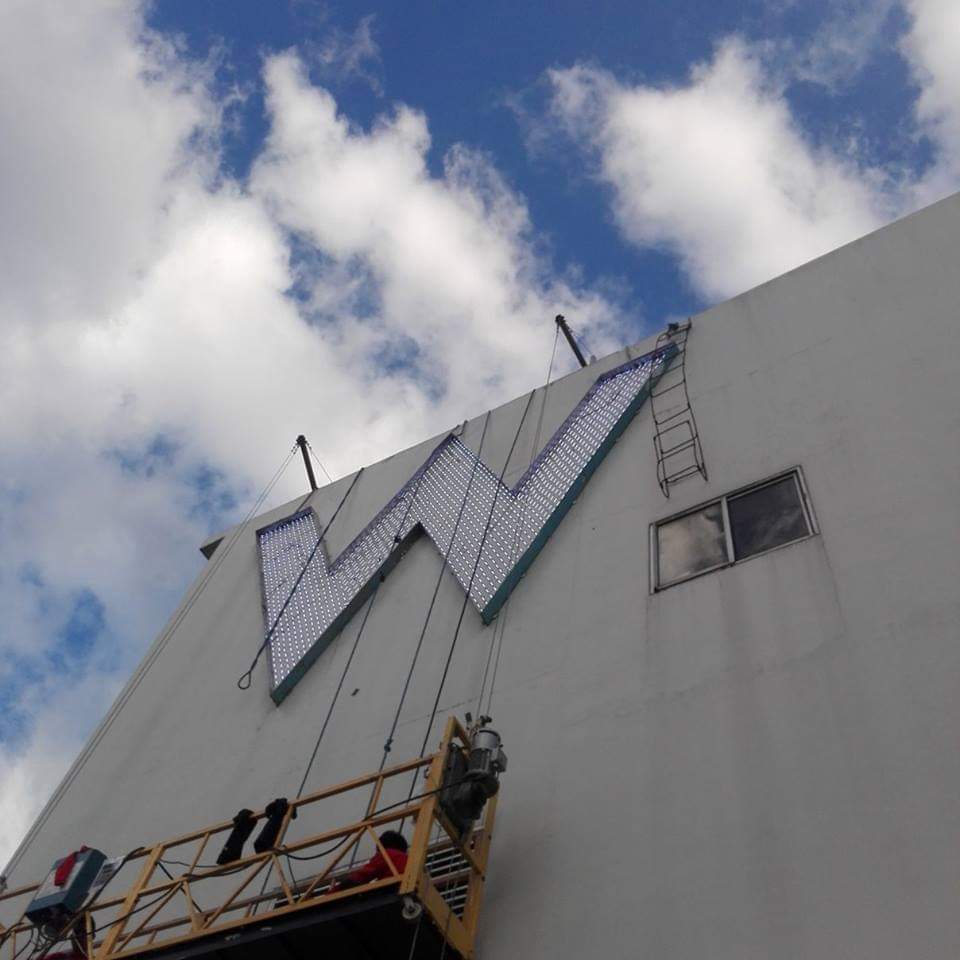 Building sign installation of a large W channel letter signage in Mandaluyong by M&G Global Ads. Workers on suspended platform.