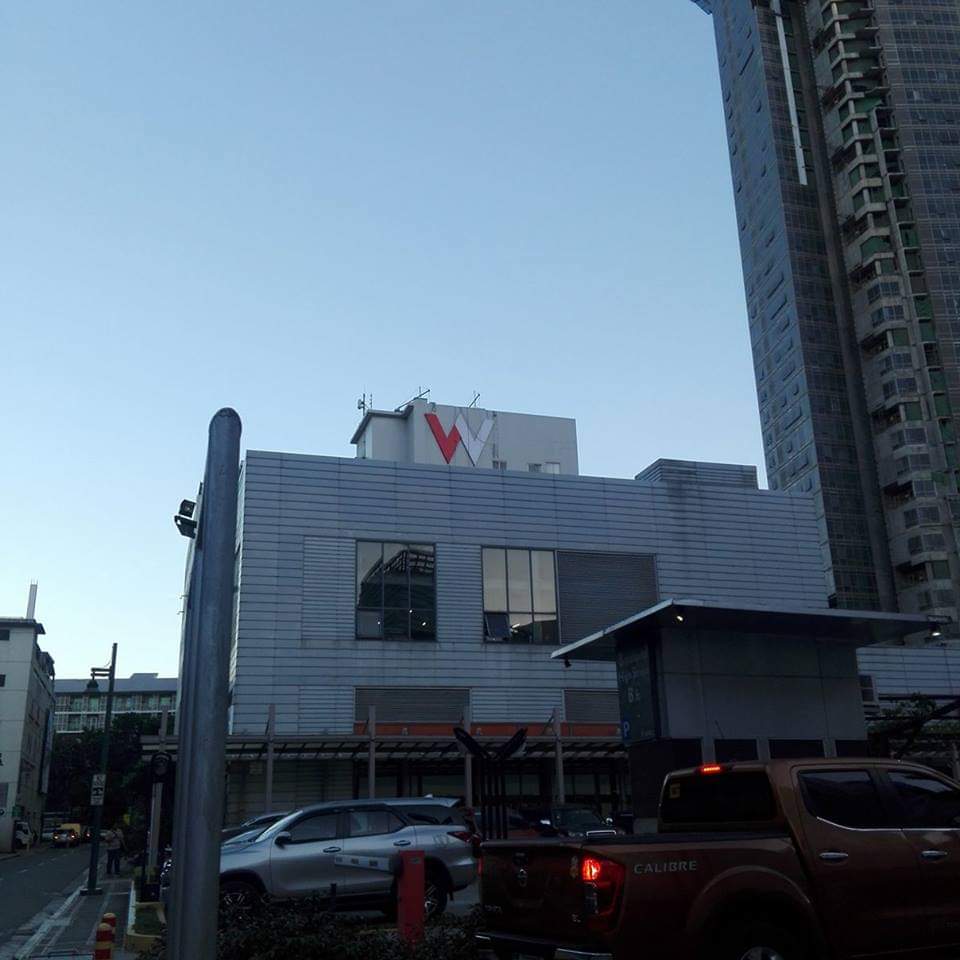 Metallic rooftop W logo signage on a modern building in Ortigas, with cityscape and vehicles, by M&G Global Ads.