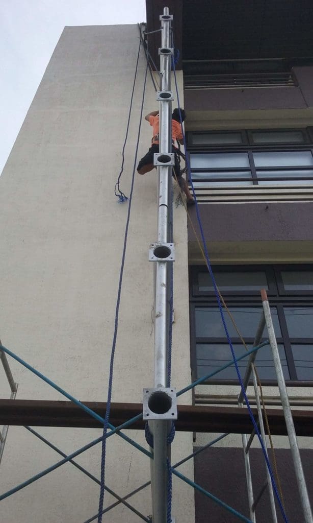 Worker in orange shirt installing stainless steel building signage via scaffolding in Makati, by M&G Global Ads.