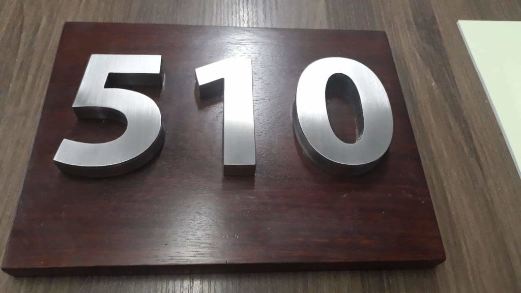 Metallic building number signage 510 on dark wood plaque in Makati, displayed on wood surface by M&G Global Ads.
