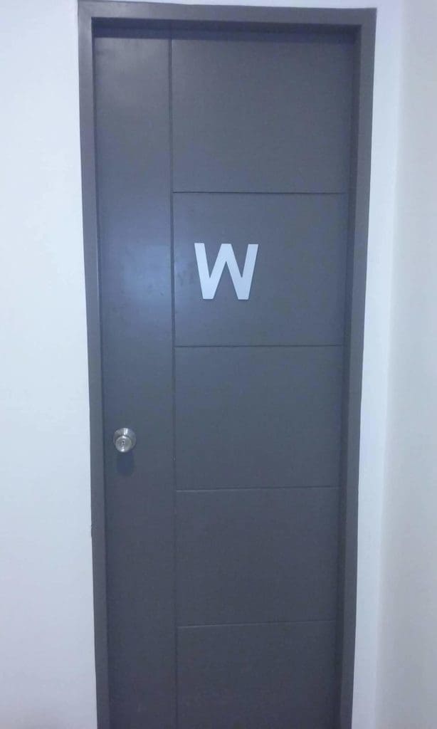 Indoor door signage with large white W and sleek silver handle in a white wall, Makati location, by M&G Global Ads.