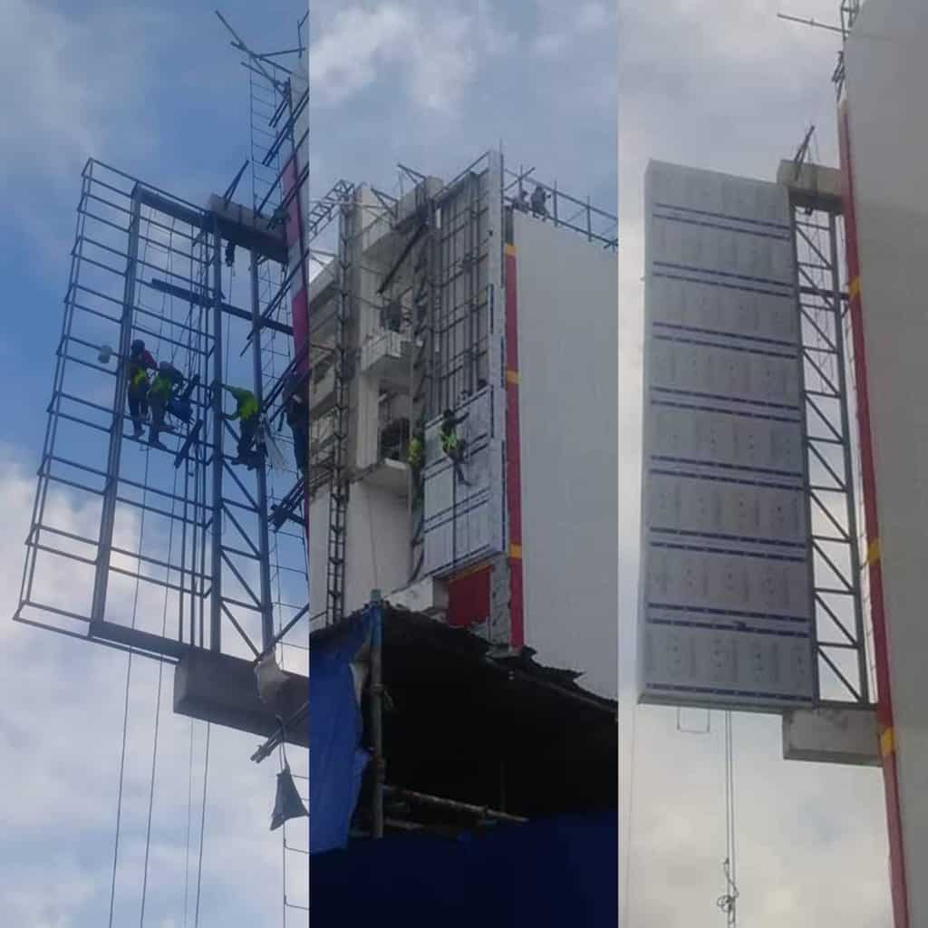 Workers installing large outdoor building signage on a tall structure in Mandaluyong, with scaffolding by M&G Global Ads.