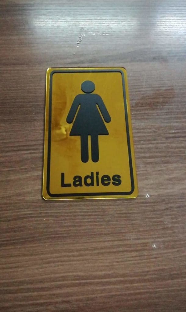 Ladies restroom outdoor sign, yellow and black metal signage in Makati with female icon on wood surface by M&G Global Ads.