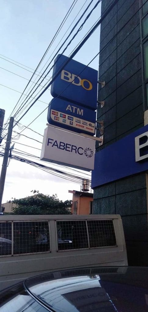 BDO ATM acrylic signage and FABERCO building signage in Quezon City by M&G Global Ads, with vehicle, wires, trees visible.