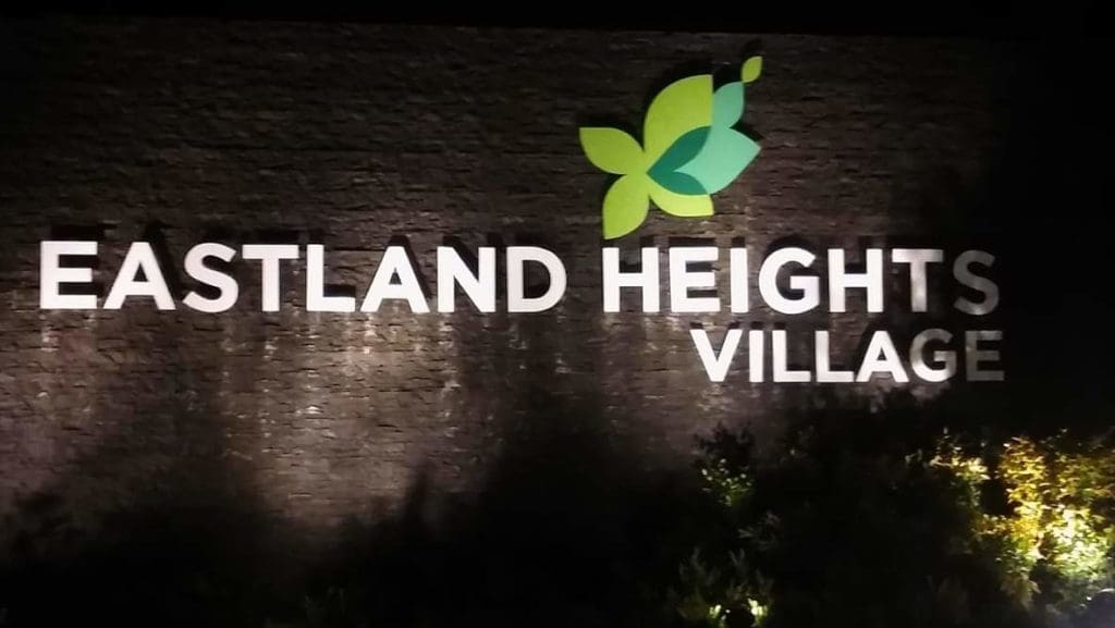 LED wall signage for Eastland Heights Village in Makati with green leaf logo and bushes, at night, by M&G Global Ads.