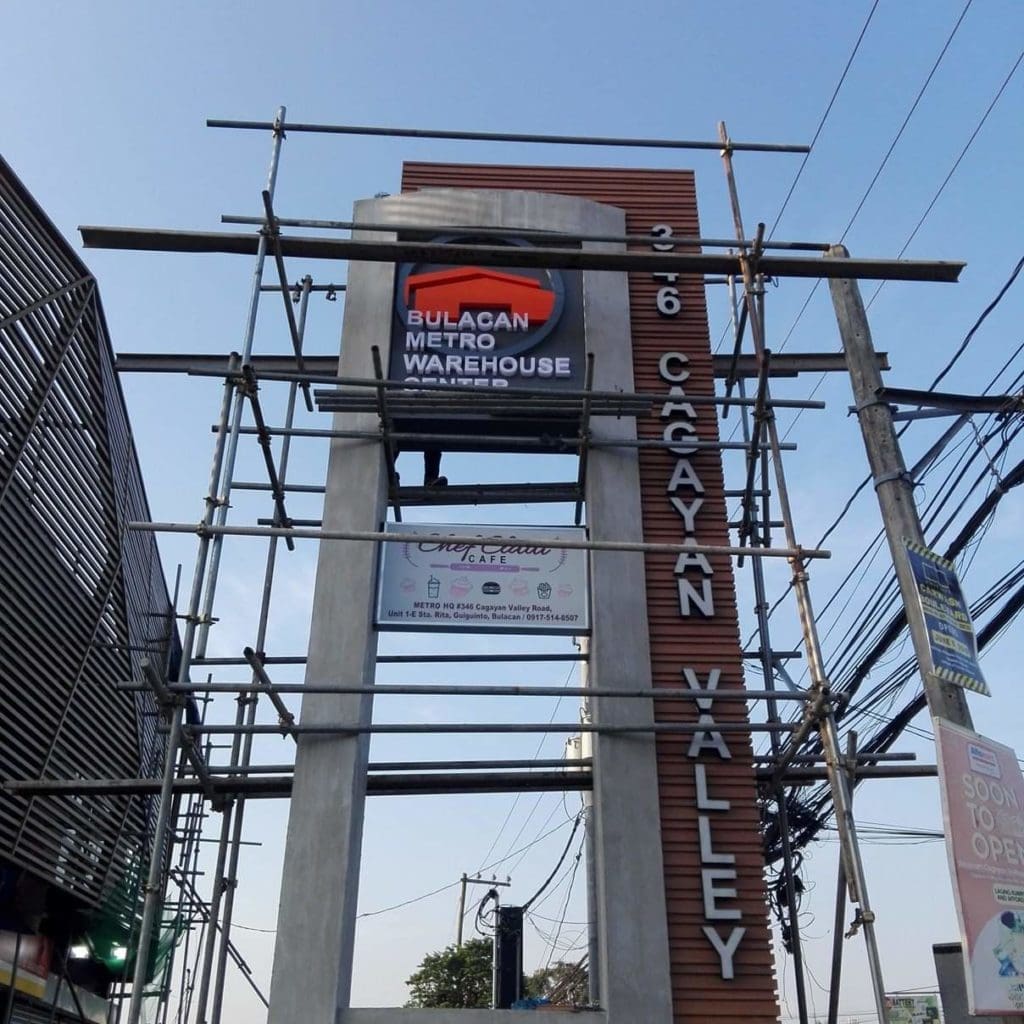 Concrete pylon signage for Bulacan Metro Warehouse, under construction in Makati, with scaffolding. By M&G Global Ads.