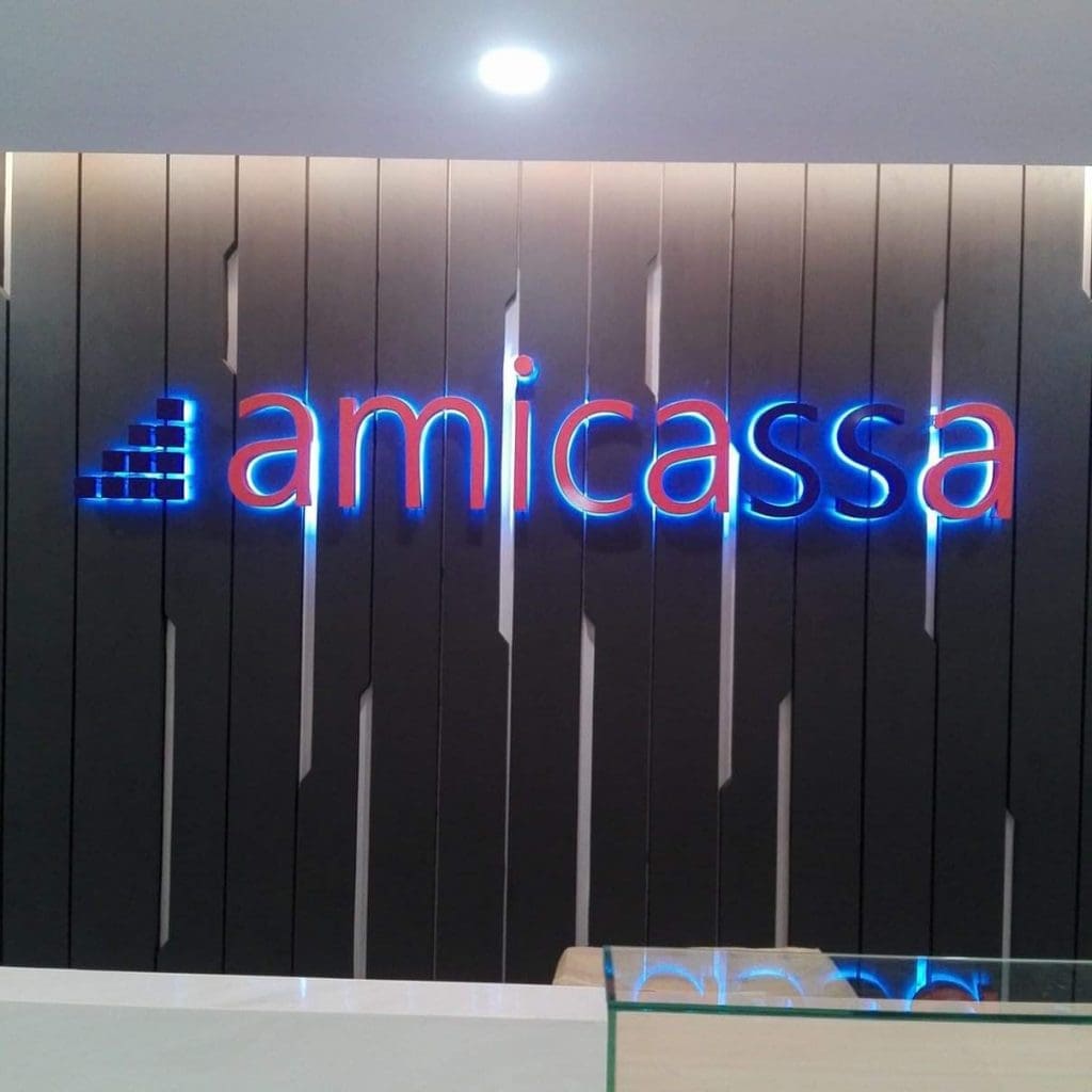 Amicassa blue and red LED signage in Makati on a dark vertical panel wall, counter with glass partition by M&G Global Ads.
