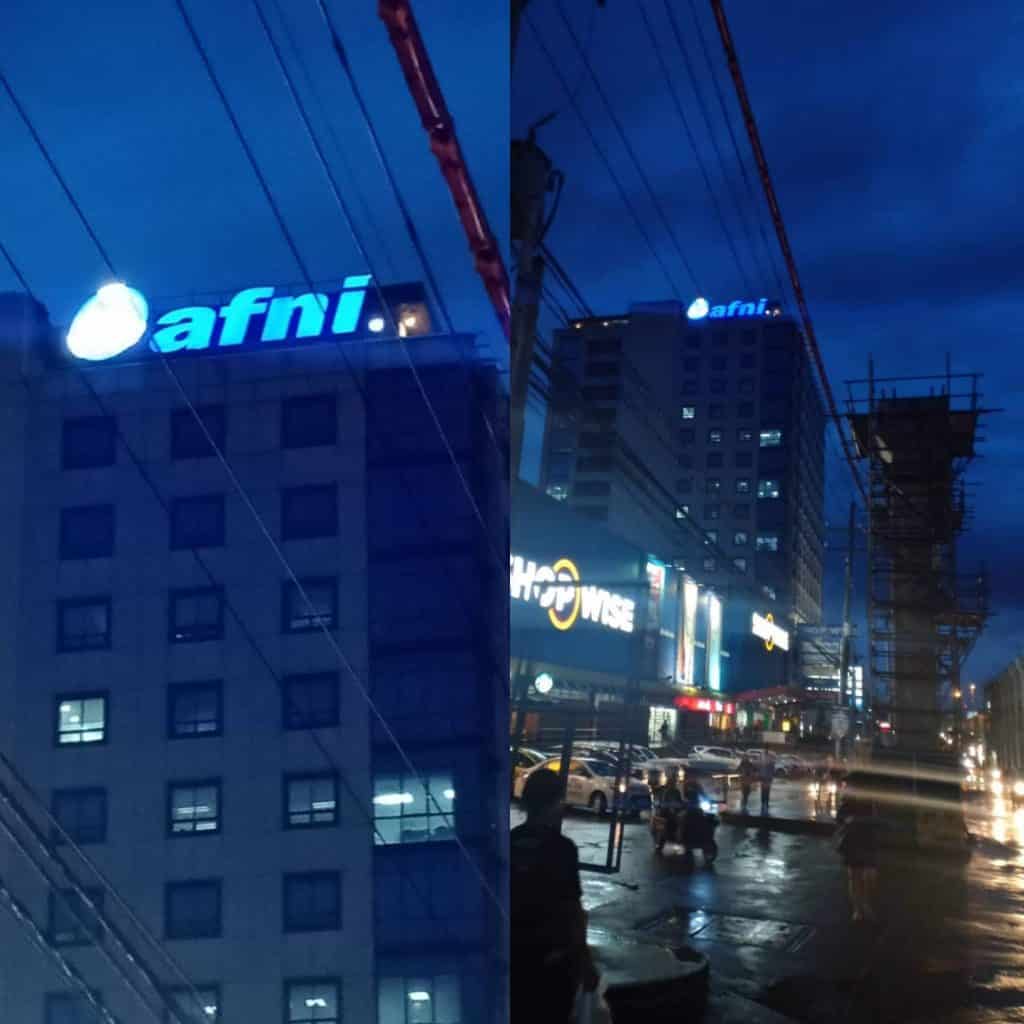 Night city view of building with blue acrylic signage in Makati, wet streets reflecting lights, by M&G Global Ads.