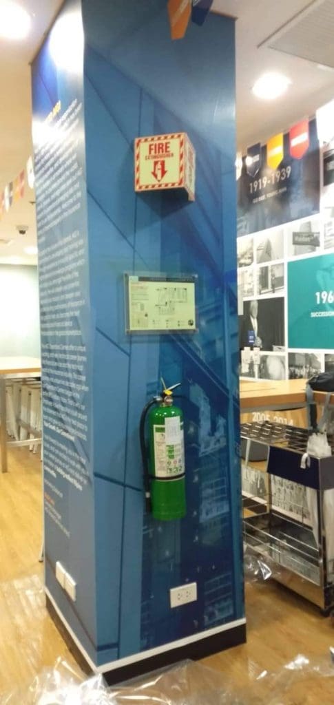 Acrylic signage on blue pillar with fire extinguisher, alarm box, outlet in Mandaluyong indoor space by M&G Global Ads.