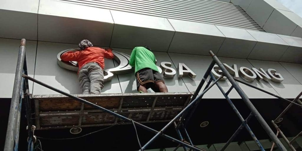 Metal sign installation for ASA GYONG in Makati, with two workers on scaffolding, by M&G Global Ads.