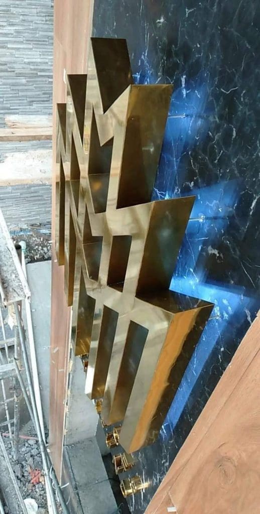 Blue LED wall signage with gold geometric sculpture on black marble, visible construction, in Makati by M&G Global Ads.