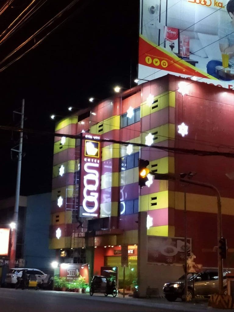 LED hotel signage glows on colorful facade in Ortigas at night, snowflake lights and cars in front; by M&G Global Ads.