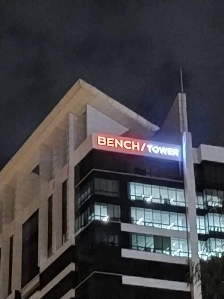 BENCH/ and TOWER illuminated LED signage on an office building in Ortigas at night, glowing lights inside, by M&G Global Ads.