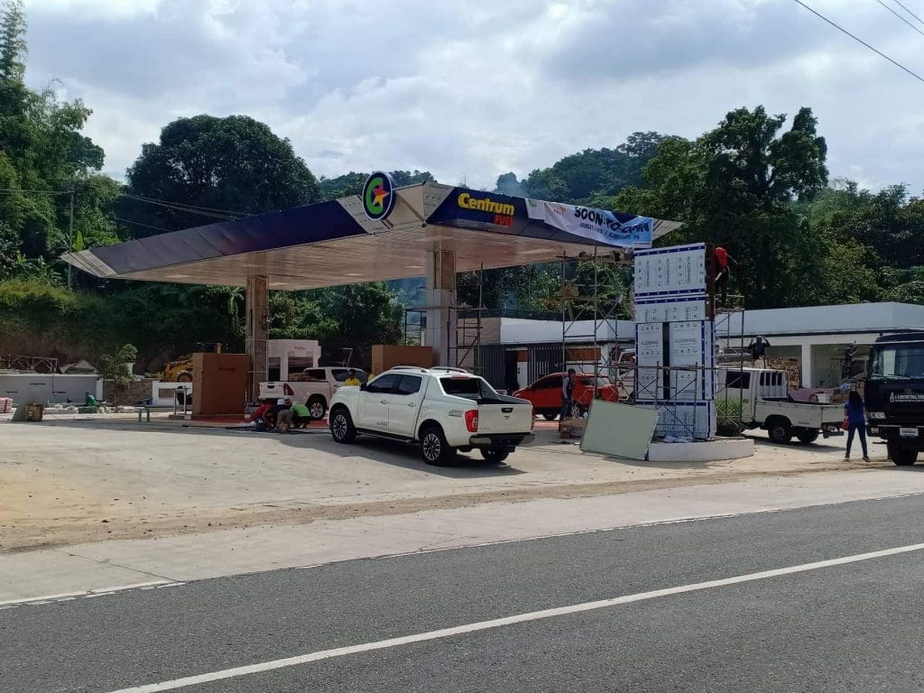 Workers install LED gas station signage for Petron in Mandaluyong, with equipment, truck, and building visible by M&G Global Ads.