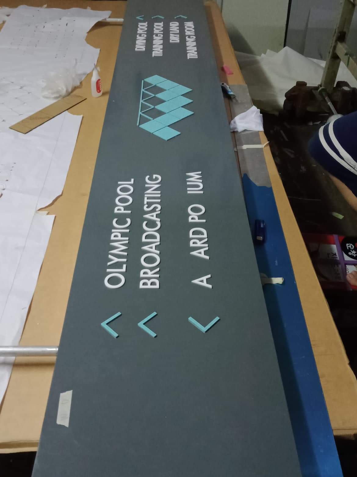 wayfinding signage for Olympic Pool Broadcasting, displayed in Makati with books and plans on table by M&G Global Ads.