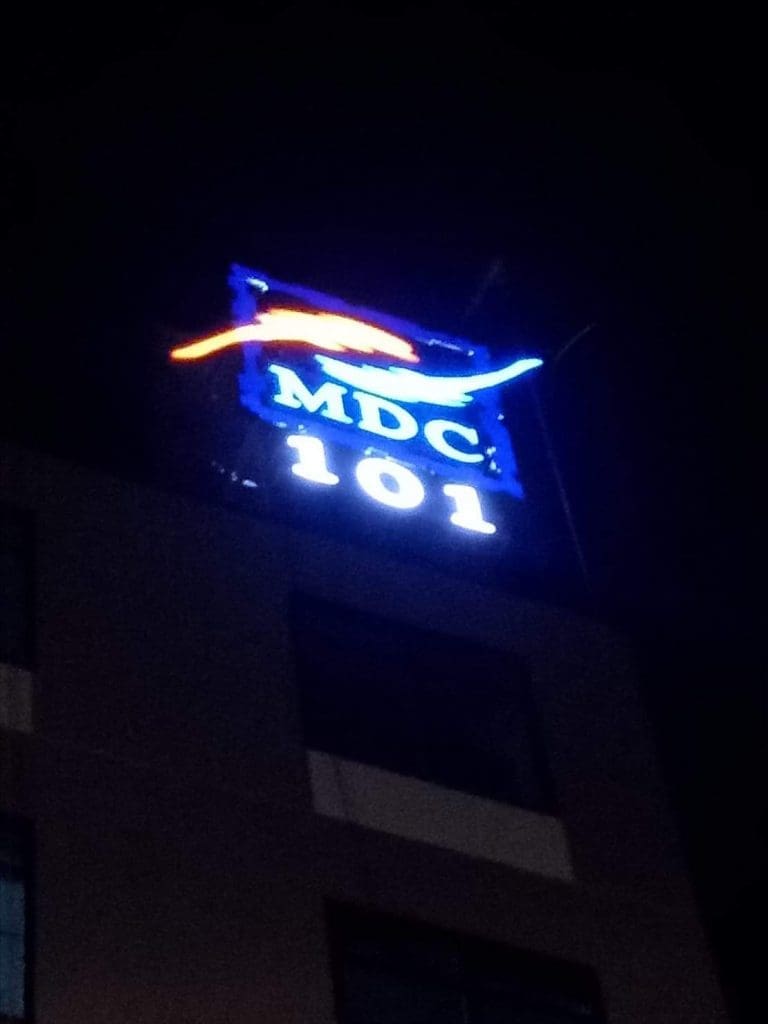 MDC 101 illuminated outdoor metal signage on a building at night in BGC, with red and blue wavy design by M&G Global Ads.