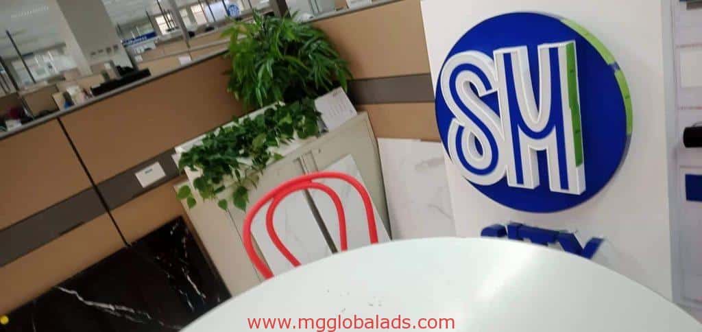 Metallic SM logo signage for SM client in Makati with red chair, white table, plants, and office cubicles by M&G Global Ads.