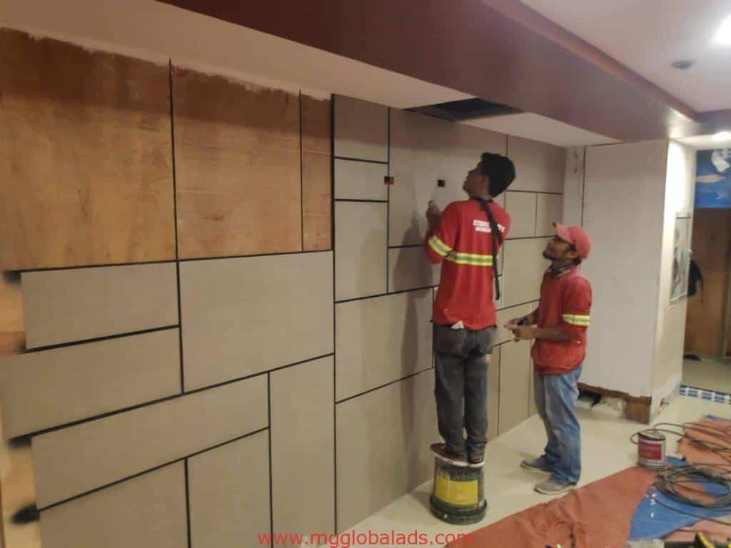 Indoor wall signage installation with geometric beige panels by workers in red shirts in Makati, by M&G Global Ads.