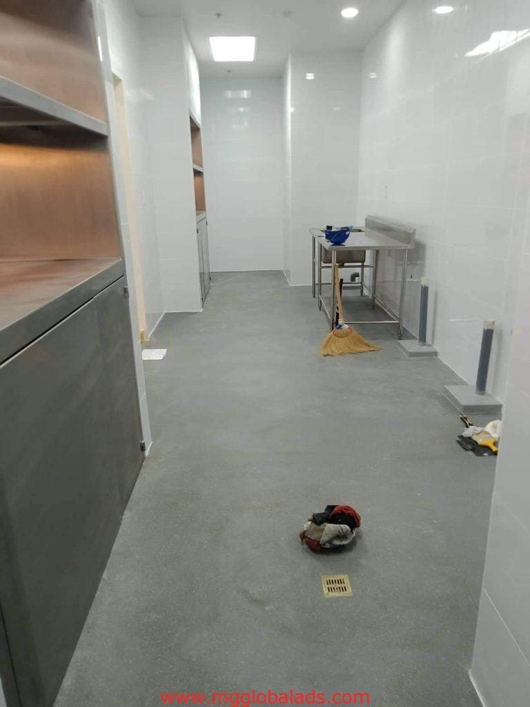 Commercial kitchen with shelves, metal table, cleaning supplies, and acrylic signage by entrance in Makati by M&G Global Ads.
