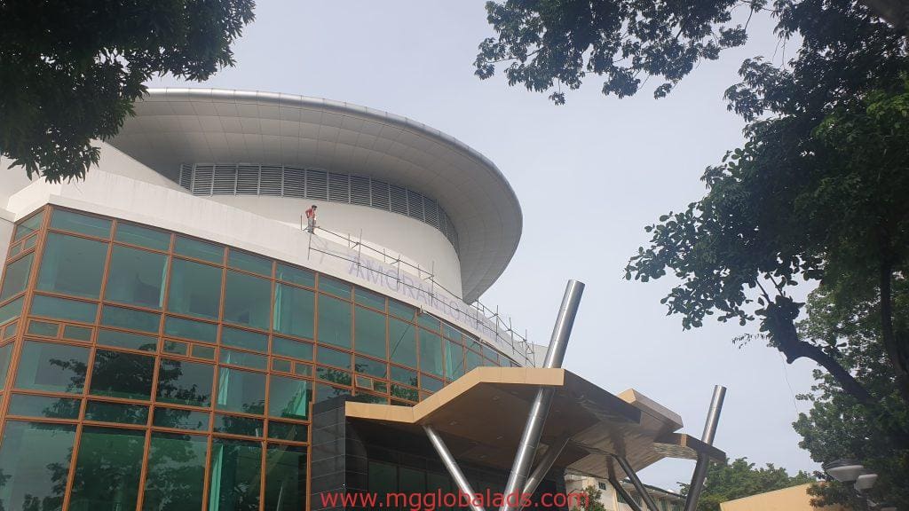 LED signage installation on modern building with green glass in Ortigas, worker on scaffolding near rooftop by M&G Global Ads.