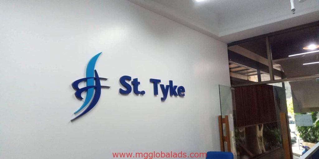 Acrylic office signage for St. Tyke in a Makati reception area, blue and white logo, glass doors, greenery—by M&G Global Ads.