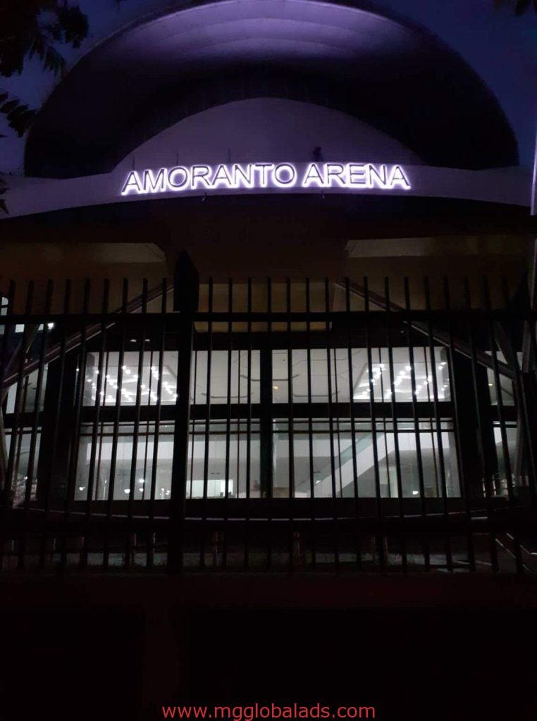 Illuminated acrylic signage for Amoranto Arena above entrance, black metal fence, Quezon City location by M&G Global Ads.