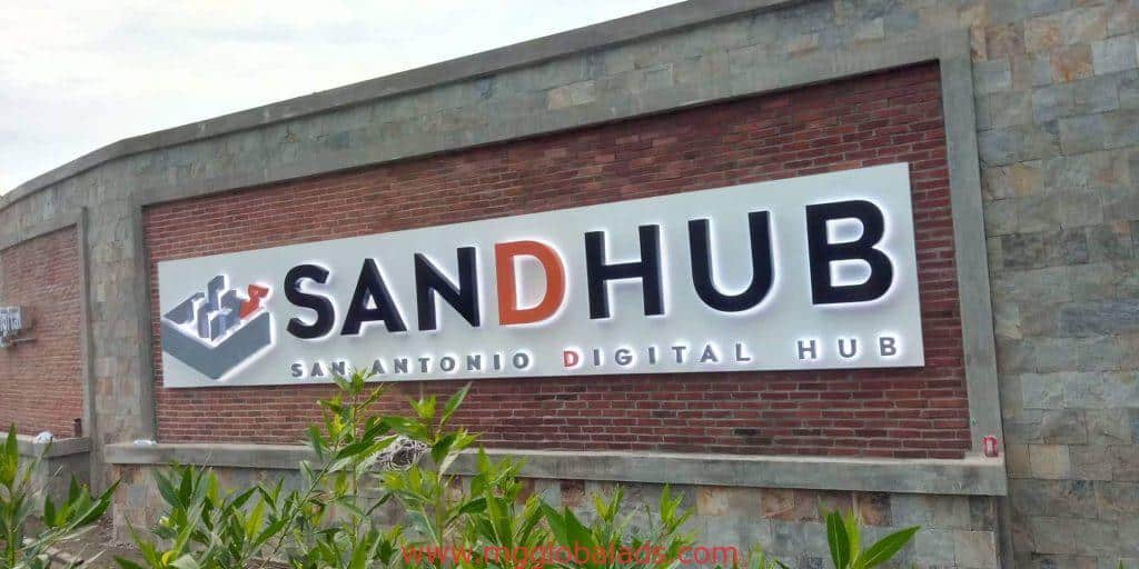 Acrylic building signage for SANDHUB in Ortigas, with orange D and check mark logo, brick wall backdrop by M&G Global Ads.
