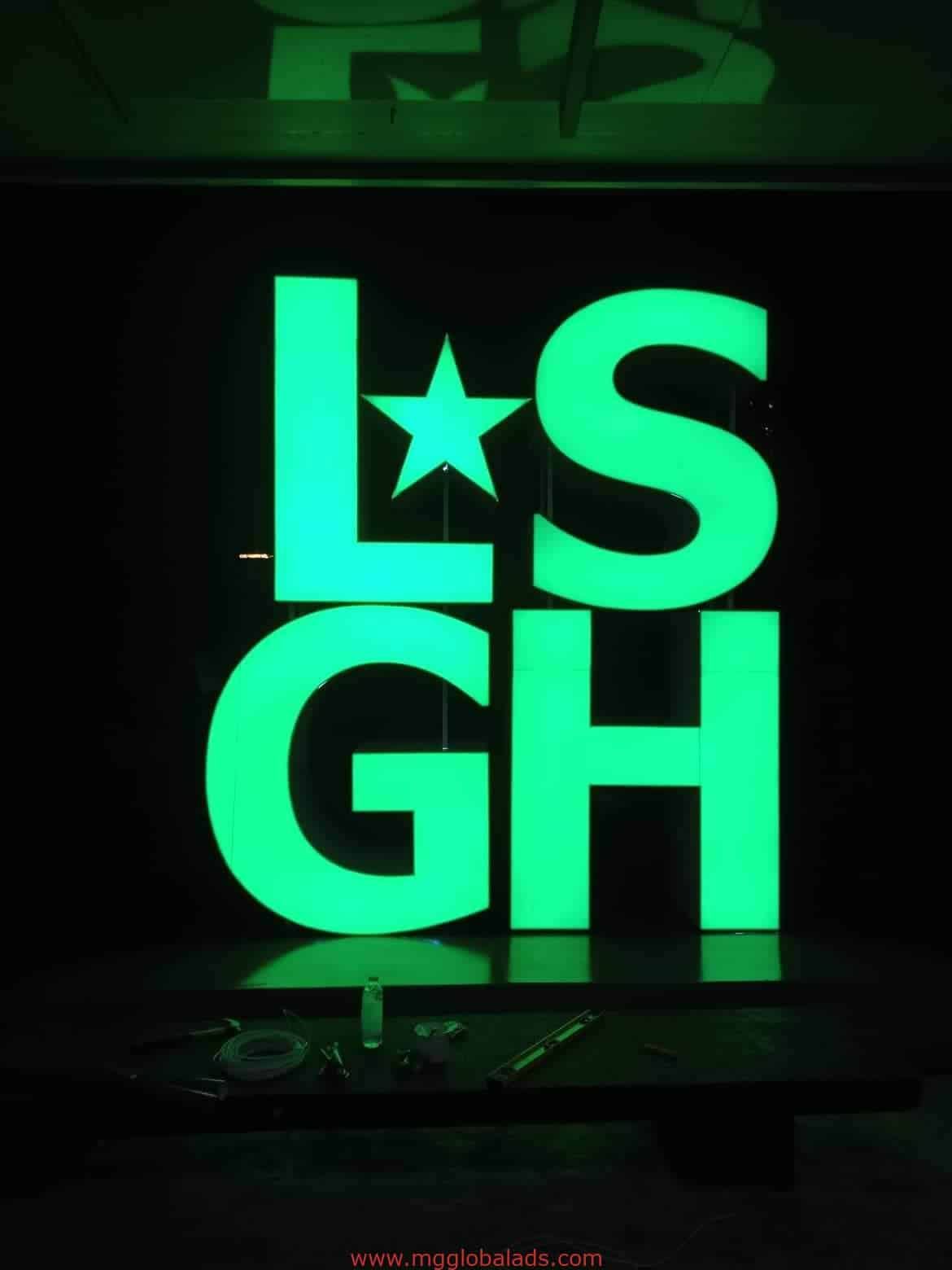 LSGH custom LED signage with star accent, lit at night in San Juan by M&G Global Ads. Some tools visible at the base.
