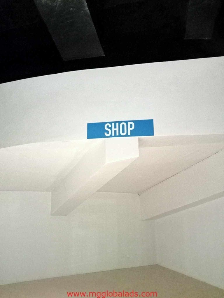 Blue metallic storefront sign with SHOP in white letters on a white wall in Makati, by M&G Global Ads.