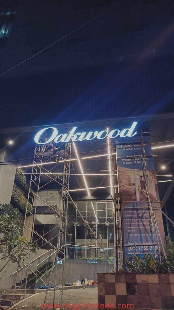 Oakwood illuminated building signage installation in Makati with metal scaffolding and banner, renovation ongoing by M&G Global Ads.