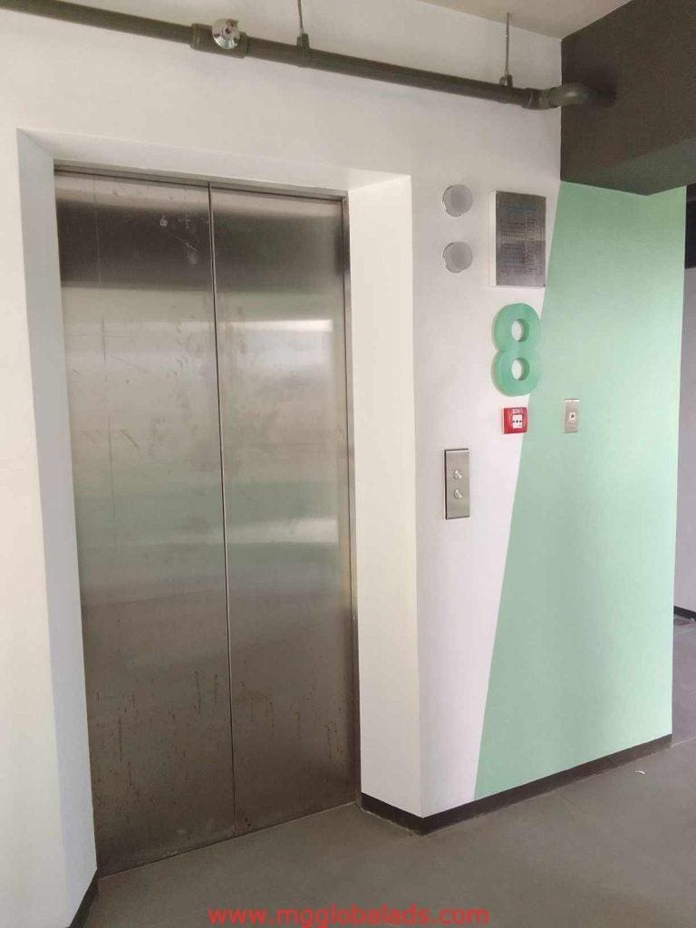 Metallic floor number signage on a stainless steel elevator door, white-mint wall, in Makati. By M&G Global Ads.