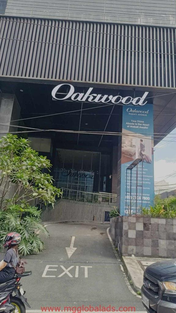 Oakwood LED signage and blue promo banner at a building entrance in Makati, exit driveway visible, by M&G Global Ads.