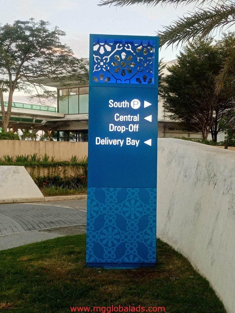 Directional outdoor signage with decorative blue patterns near curved road in Makati, showing drop-off points, by M&G Global Ads.