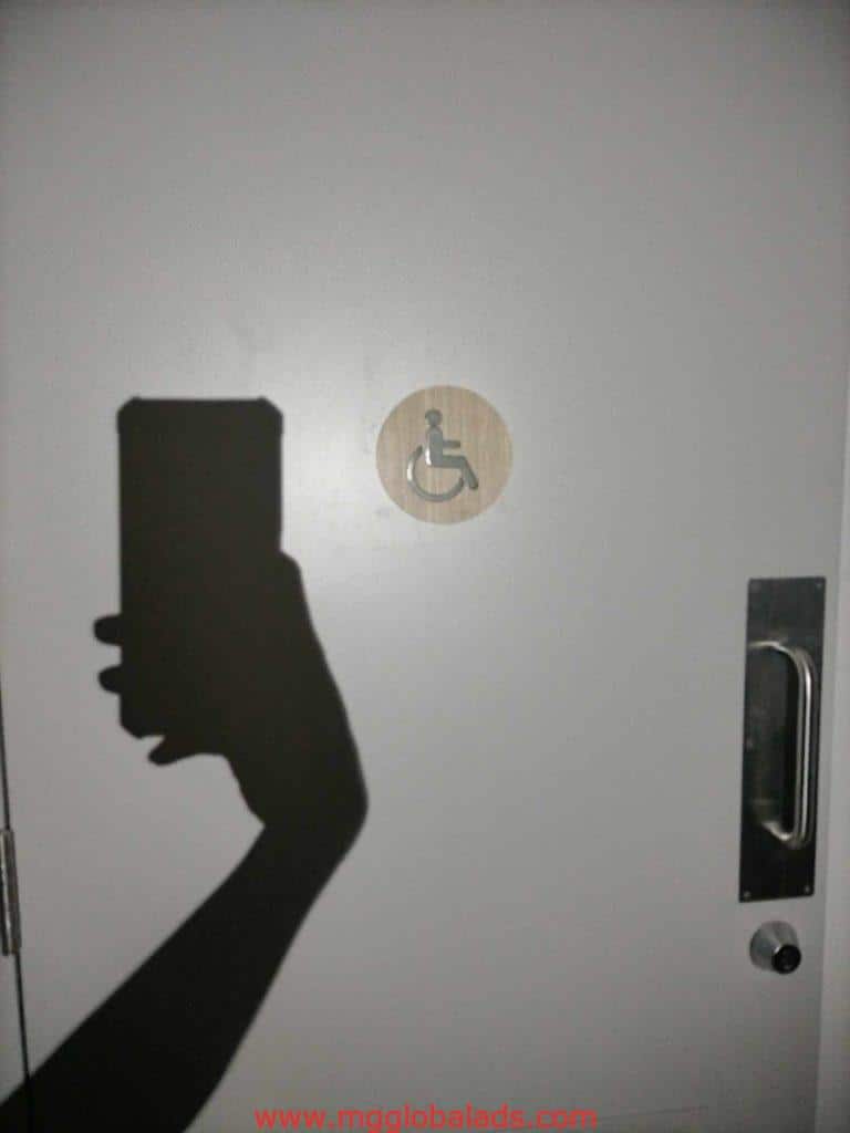 Wheelchair accessibility round signage on a white door in Makati, metal handle right side. Photo by M&G Global Ads.