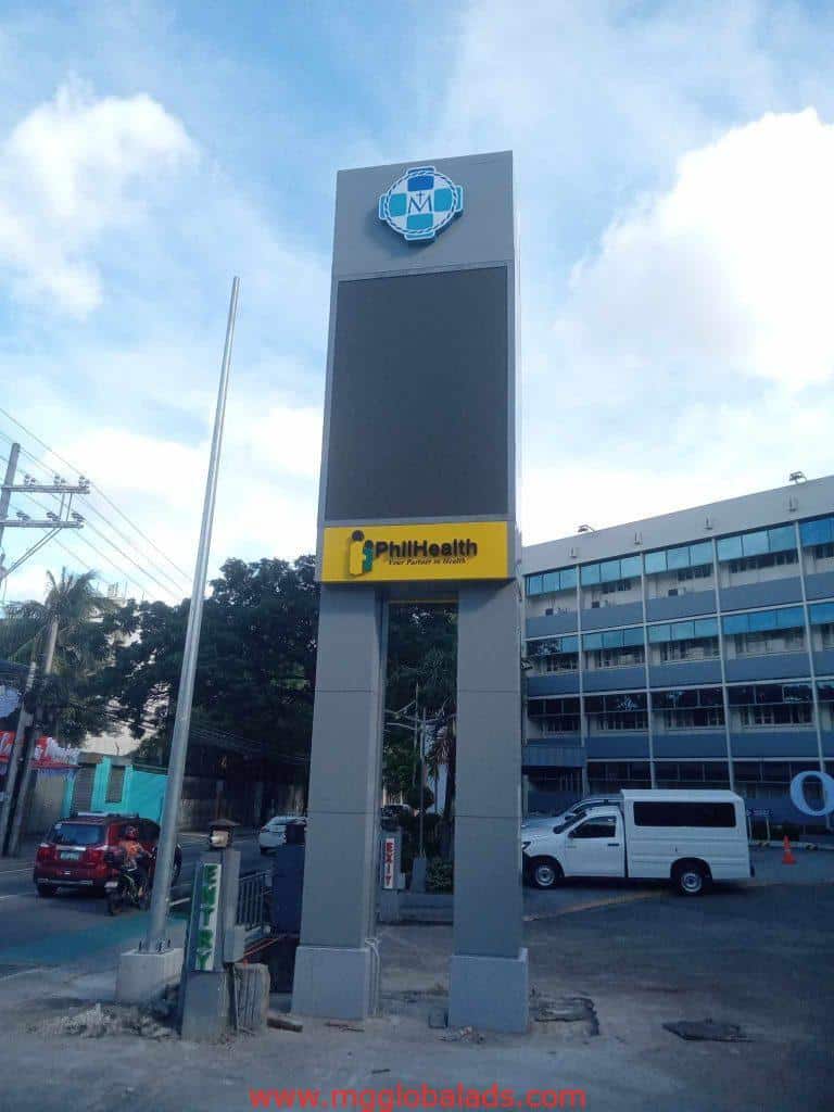 Digital pylon signage SM Mall and PhilHealth, parking lot in Makati, cars and buildings visible, by M&G Global Ads.