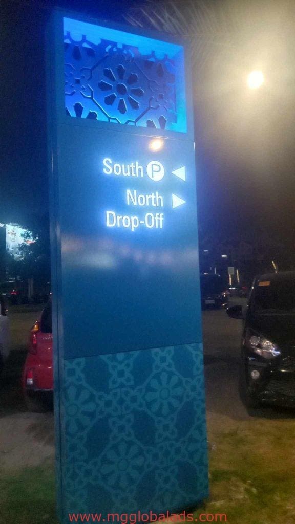 Directional wayfinding sign with arrows for South P and North Drop-Off in Makati at night, cars parked nearby by M&G Global Ads.