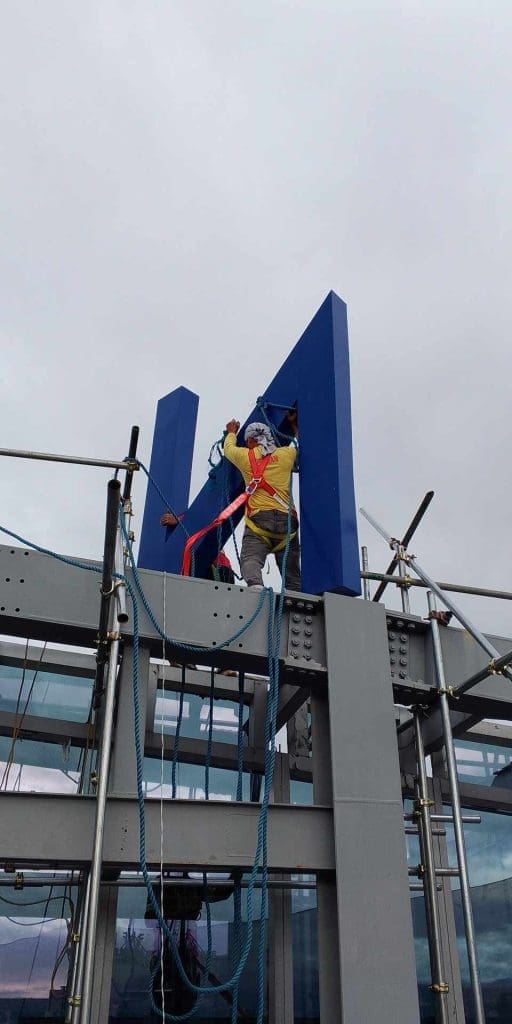 Installing large 3D metal channel letter signage M in Makati, construction worker on scaffolding. By M&G Global Ads.