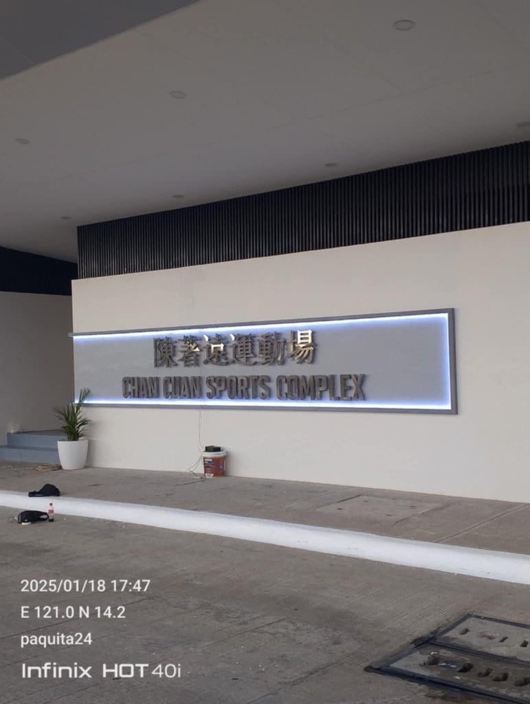 Outdoor building signage for CHAN CHAN SPORTS COMPLEX on a white wall in Ortigas by M&G Global Ads. Tools and paint can nearby.