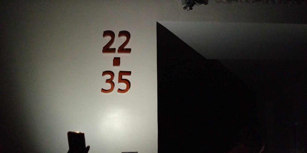 22/35 acrylic signage displayed on a dim wall, phone glowing in foreground, Makati installation by M&G Global Ads.