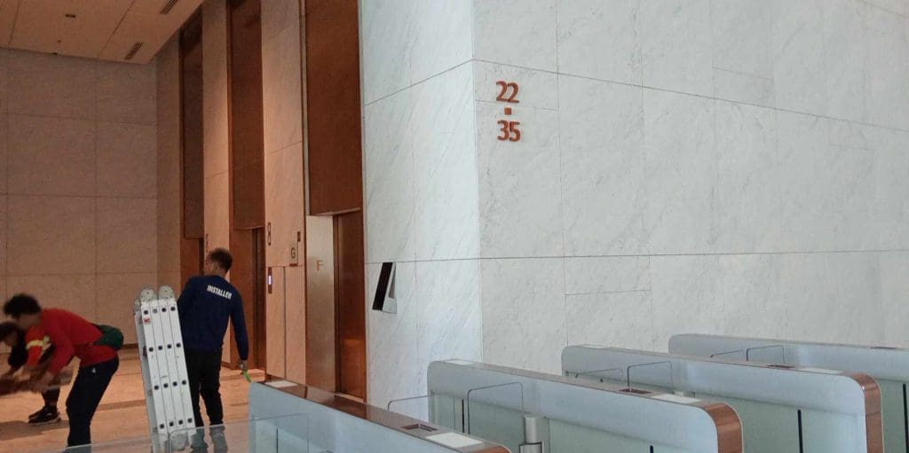 Acrylic signage installation near elevators in modern Makati lobby with marble walls, floor indicators, by M&G Global Ads.