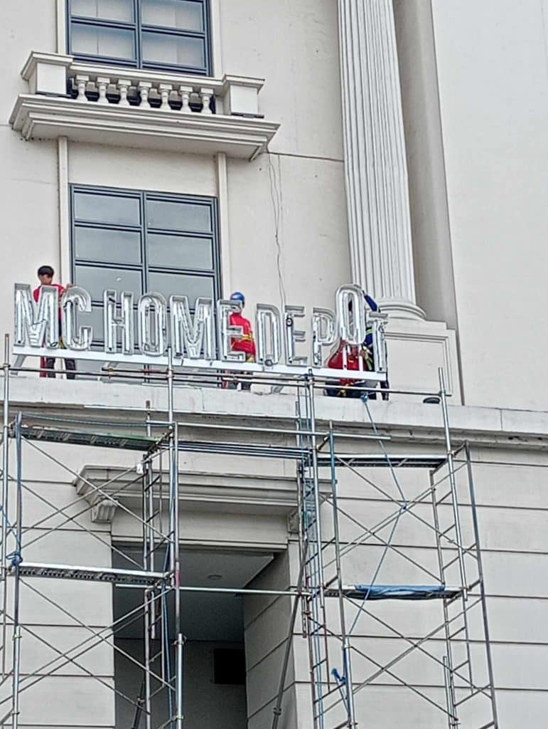 MC HOME DEPOT acrylic building signage installation in Mandaluyong, workers on scaffolding, sign missing last letter by M&G Global Ads.