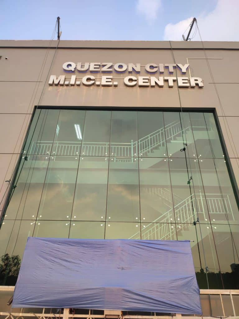 Quezon City M.I.C.E. Center metallic building signage with white letters in Quezon City, blue tarp at entrance by M&G Global Ads.