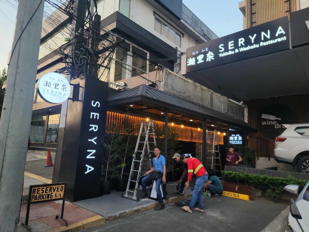 Workers install illuminated LED signage for Seryna Japanese restaurant in Makati, with ladder and parking sign, by M&G Global Ads.