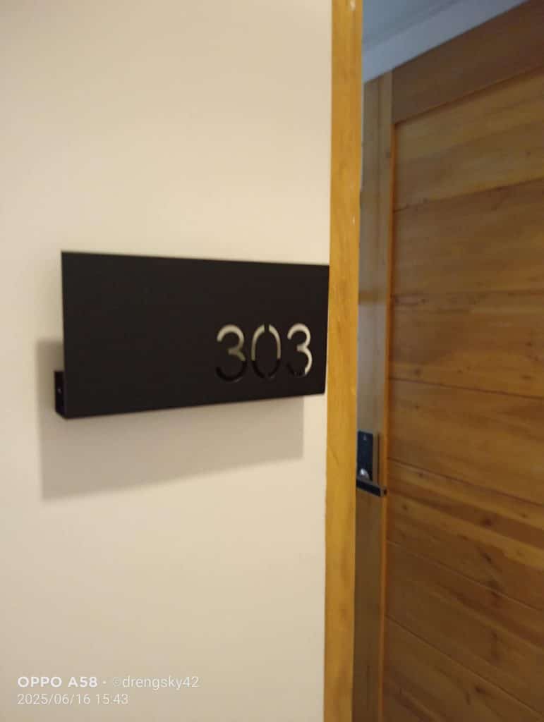 Room number signage “303” in black metallic cut-out style on a white wall beside a wooden door in Ortigas by M&G Global Ads.